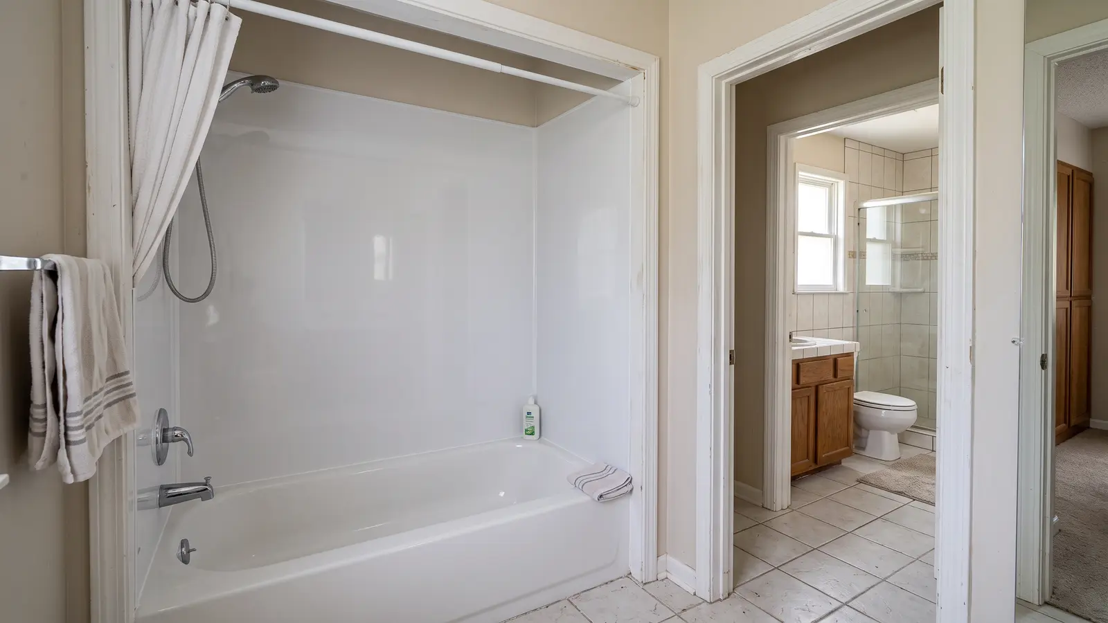 Lexington bathroom showing a one-piece acrylic tub surround beside a fully remodeled tiled bath with a new vanity