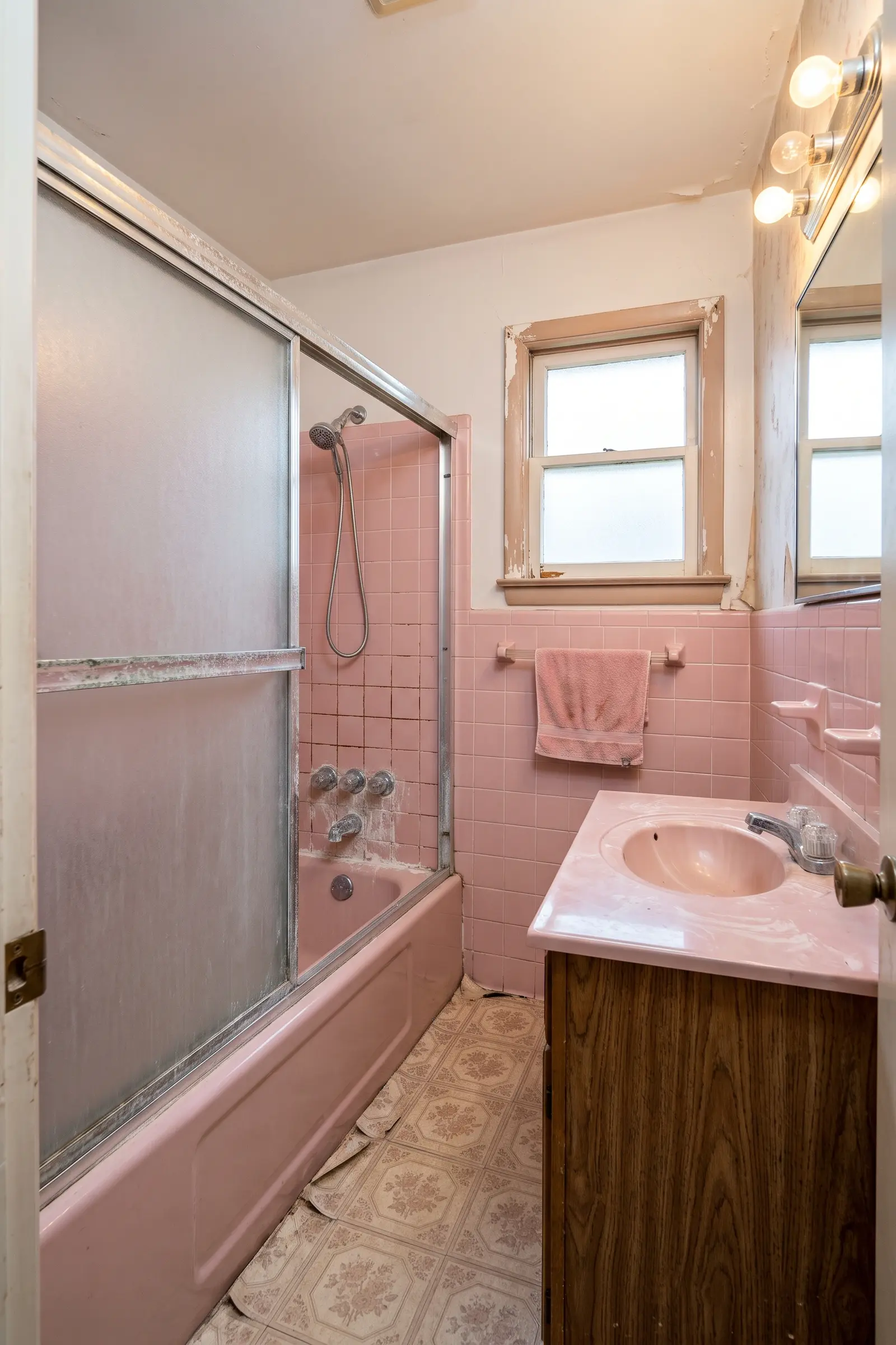 Dated pink tile bathroom with a sliding glass tub door and worn vinyl floor